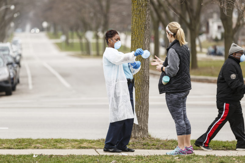 Milwaukee, WI - APRIL 7th: A woman hands out surgical masks to people standing in line to vote in Wisconsin’s spring primary election on Tuesday April 7th, 2020 at Riverside High School in Milwaukee, WI. (Photo by Sara Stathas for the Washington Post)